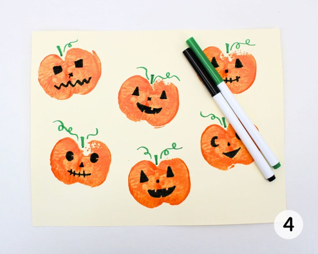 Apple stamped pumpkin craft with jack-o'-lantern features, stems and vines added.
