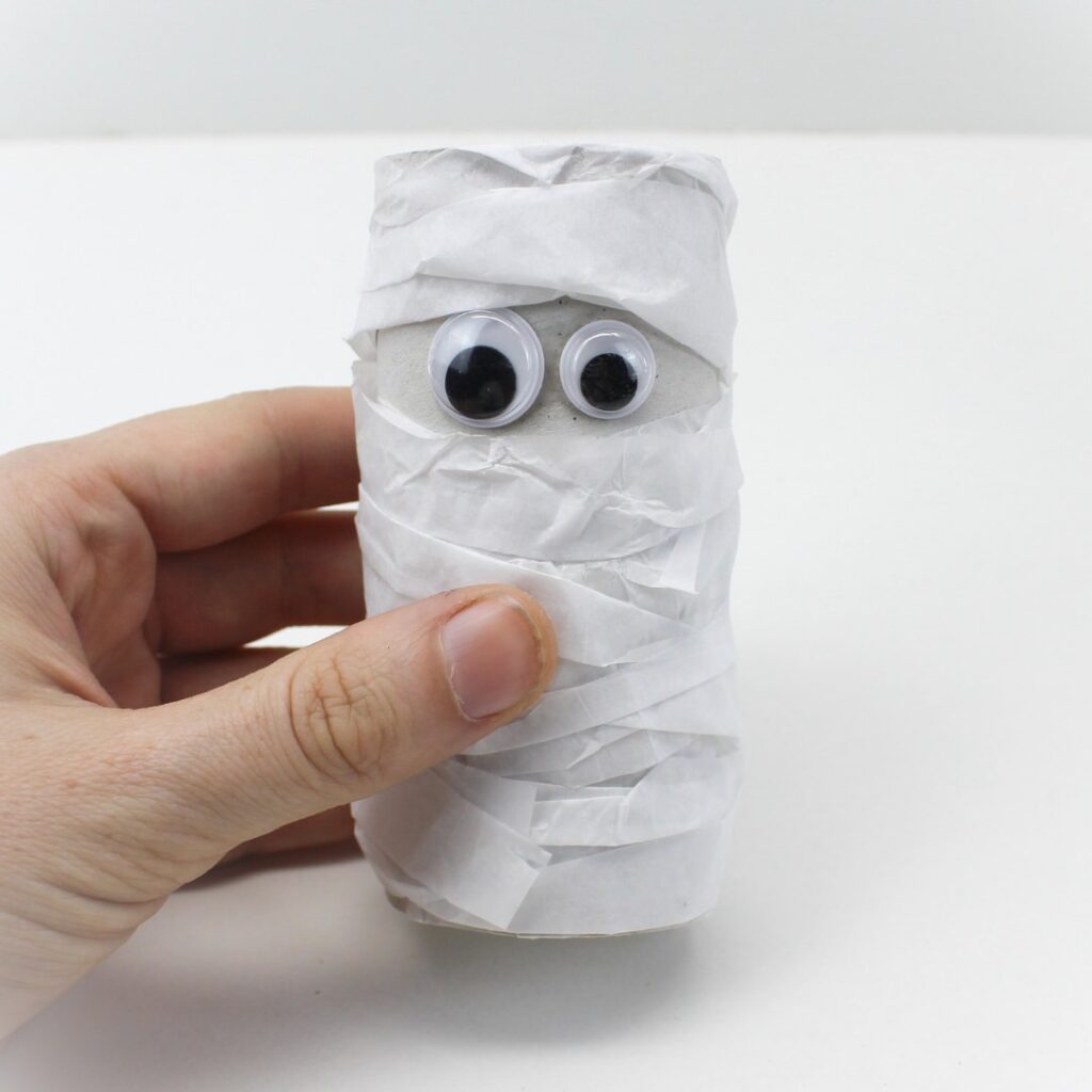 Hand holding tissue-paper wrapped paper roll mummy craft.