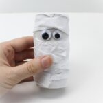 Hand holding tissue-paper wrapped paper roll mummy craft.