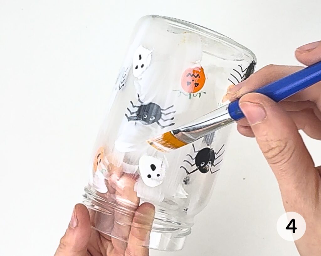 Hands covering the glass jar with Mod Podge.