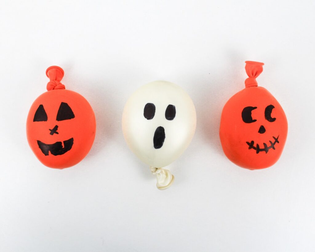 Jack-o'-lantern and ghost stress balls on a white table.