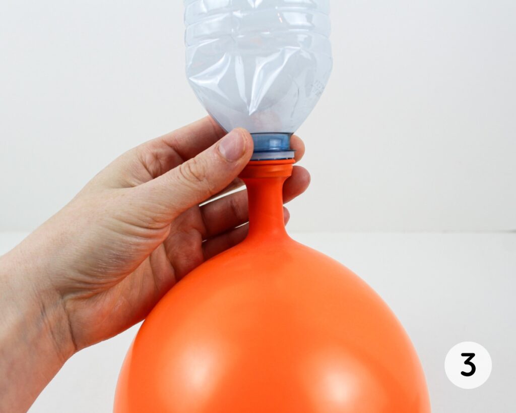 Upside down water bottle pouring flour into an inflated orange balloon.