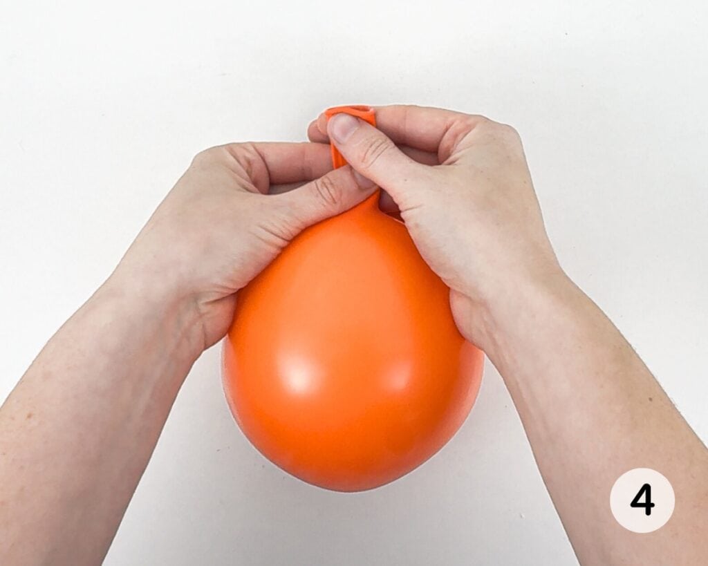 Hands holding an orange balloon and allowing it to deflate.