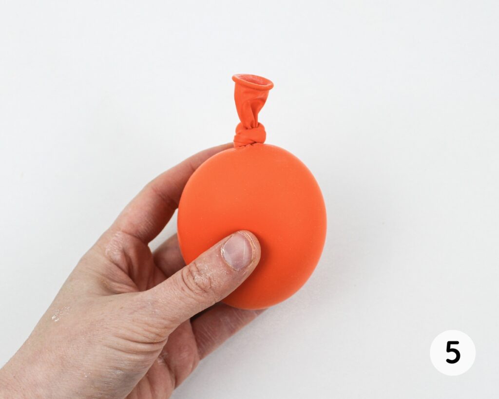 Hand holding a tied orange balloon filled with flour.