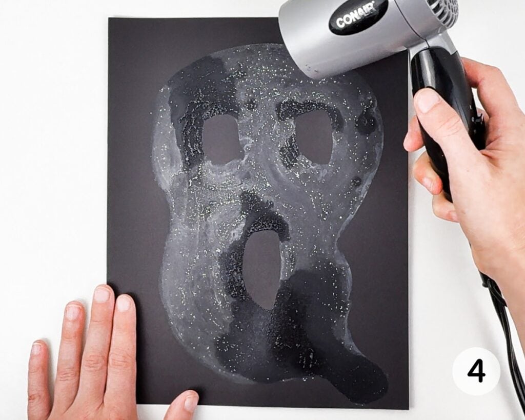 Hands drying the ghost to make it appear white on black cardstock.