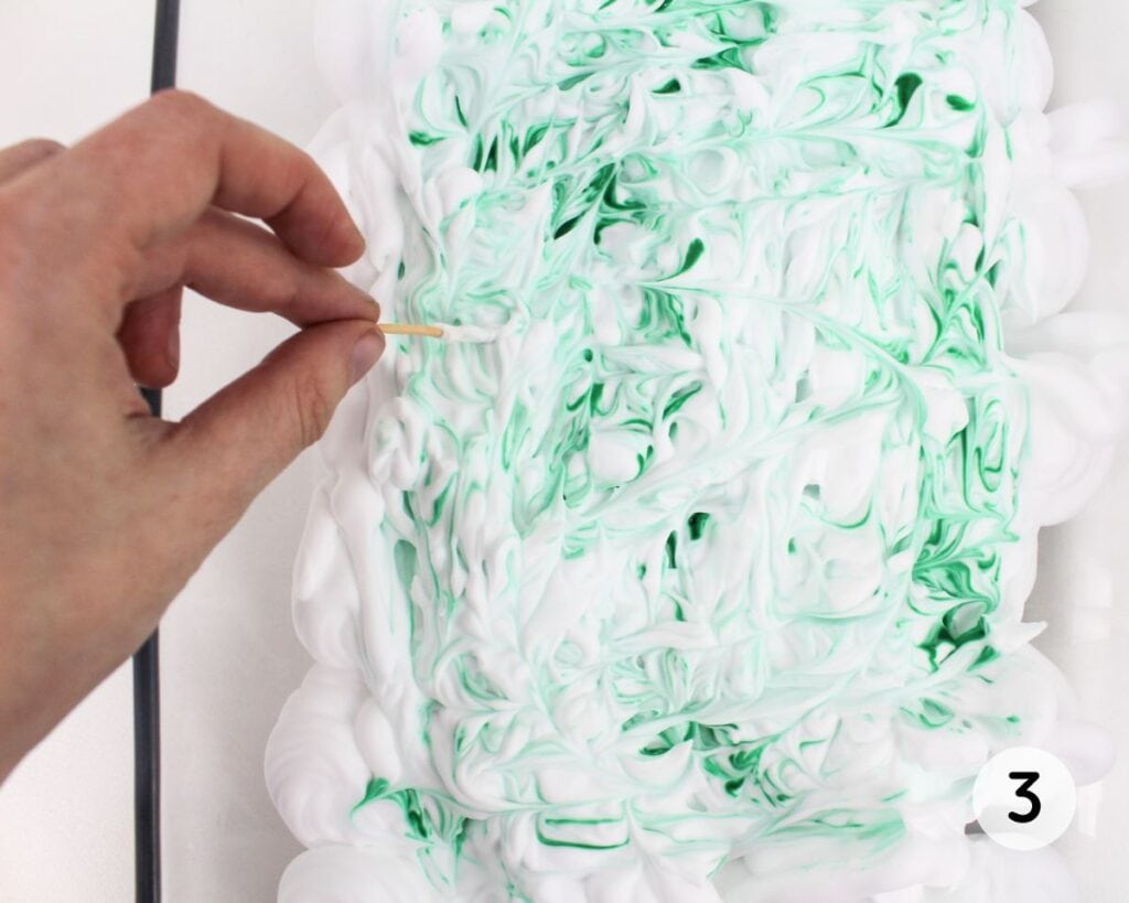 Hand swirling food coloring with a toothpick.