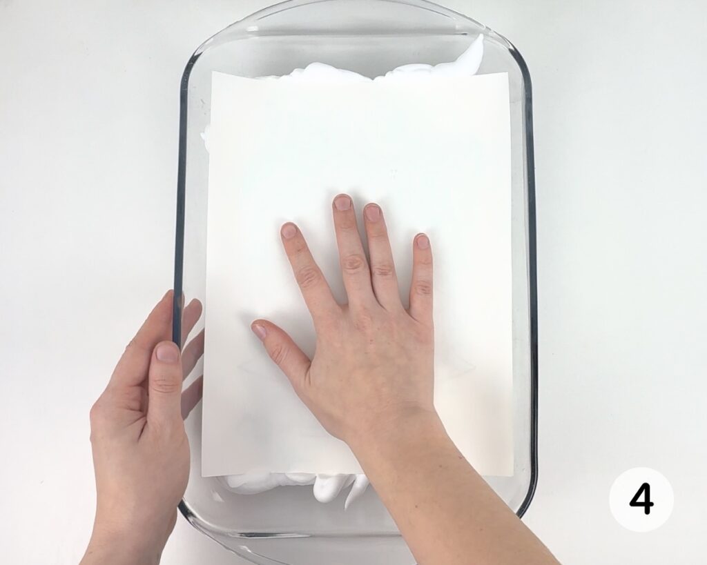 Hand pressing a sheet of white cardstock onto the shaving foam.
