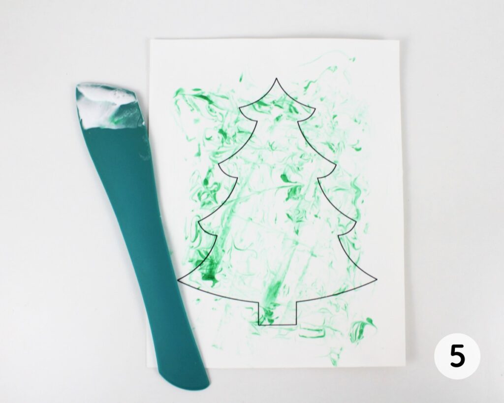 Colored shaving cream being scraped off a Christmas tree template.