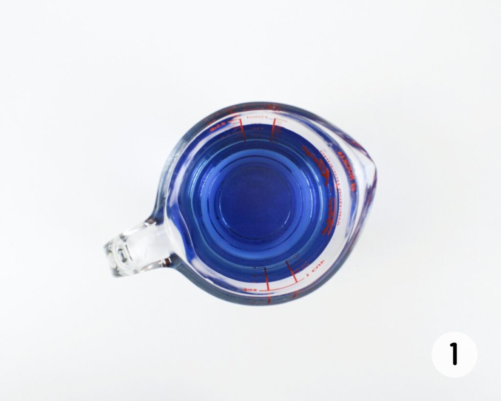 Glass measuring cup filled with blue water.