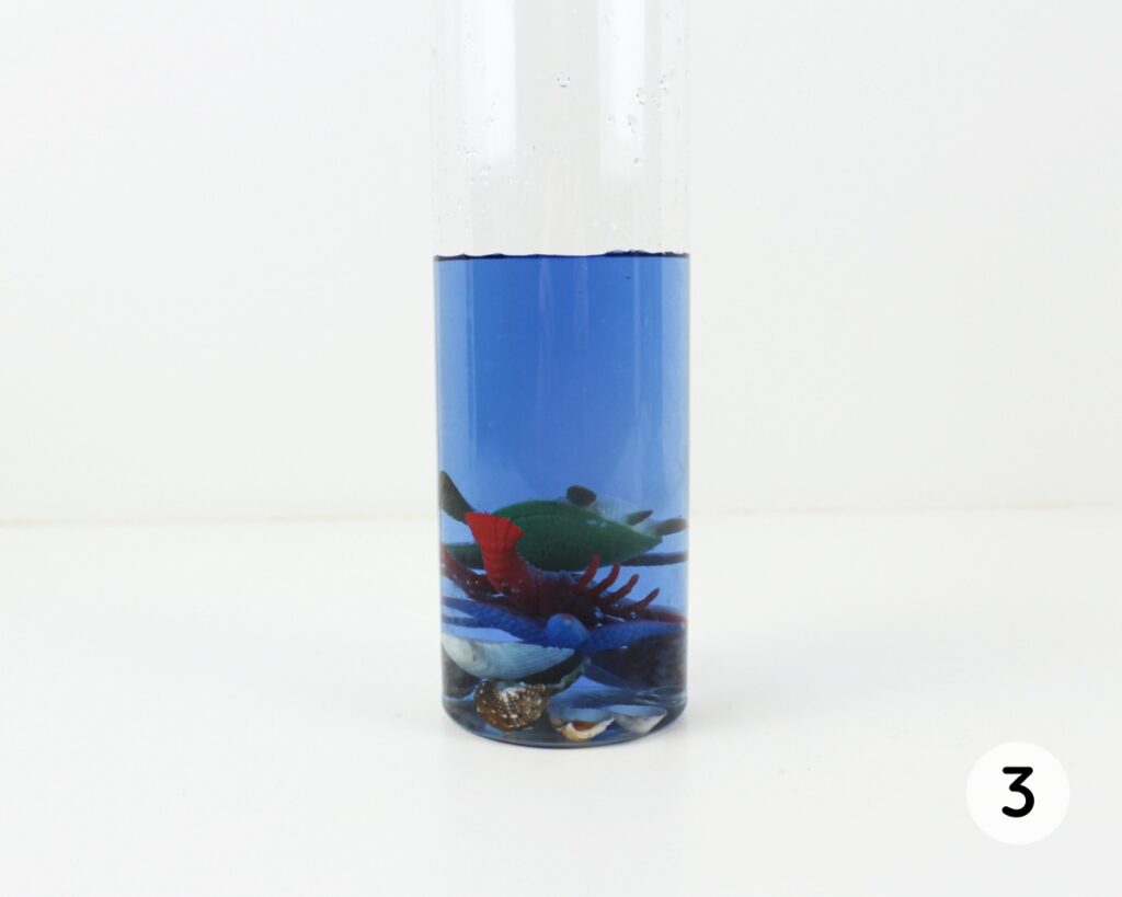 Bottle with blue water, ocean toys and seashells inside.