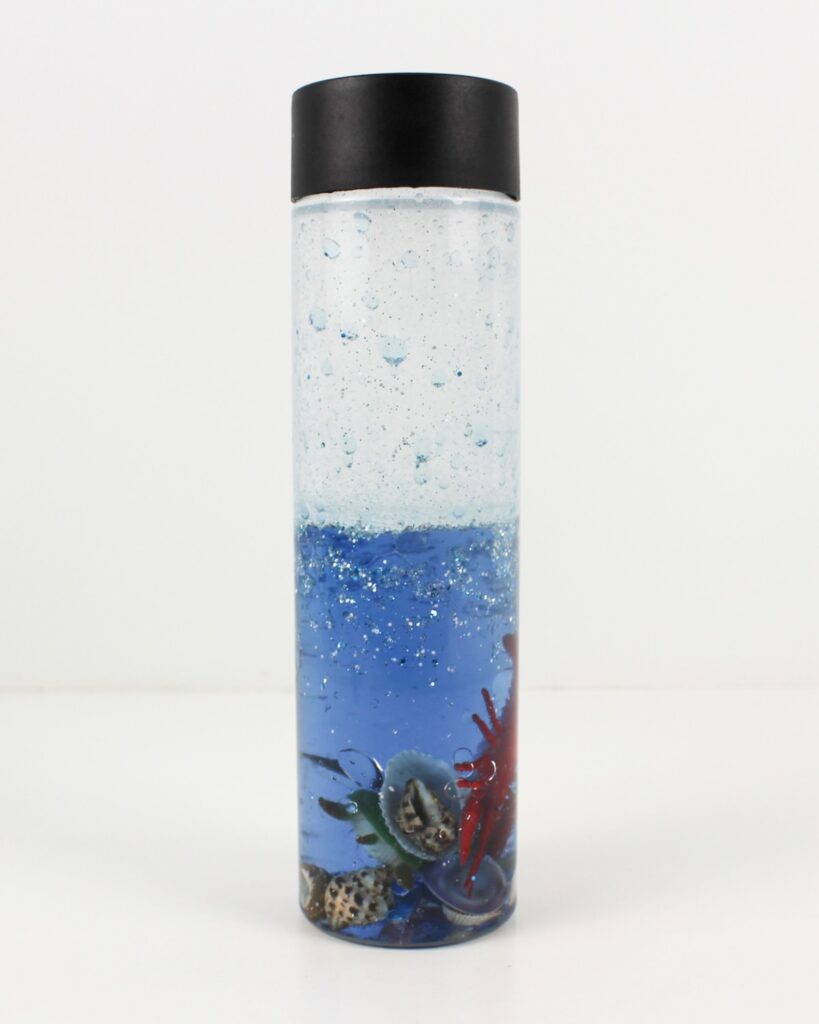 Ocean sensory bottle with blue water, glitter, seashells and ocean toys.