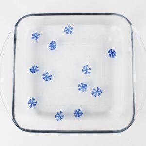 Floating blue snowflake drawings inside a glass dish with water.