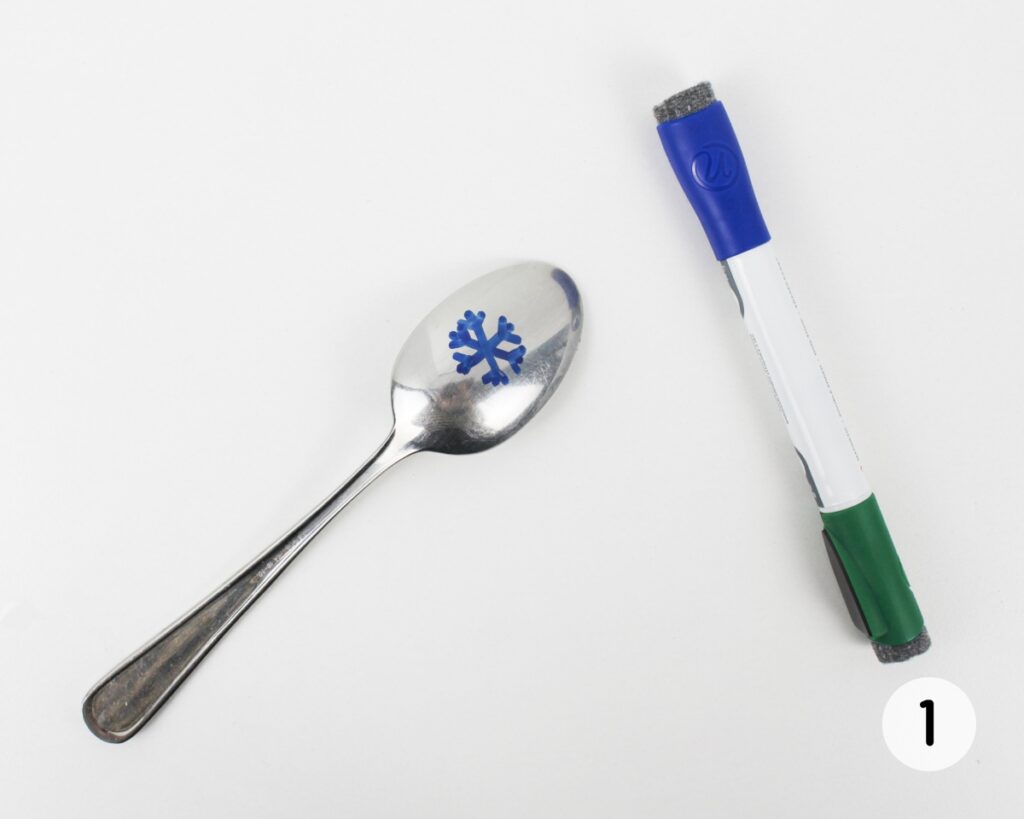 Blue snowflake drawing on the back of a metal spoon.