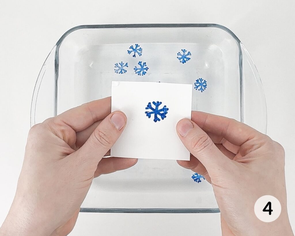 Hands holding up a small piece of paper with a blue snowflake drawing.