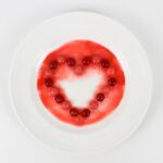 Skittles, arranged in the shape of a heart on a small plate, with the colors leaching out.