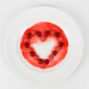 Skittles, arranged in the shape of a heart on a small plate, with the colors leaching out.