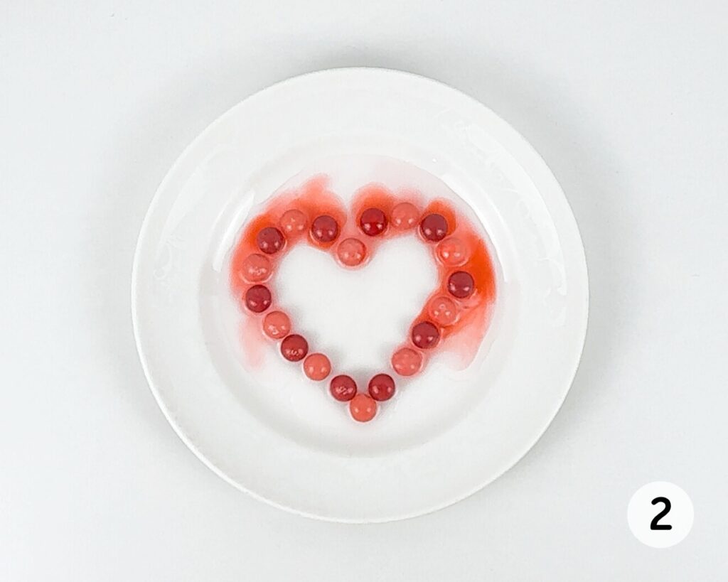 Skittles, arranged in the shape of a heart on a small plate, with the colors beginning to leach out.