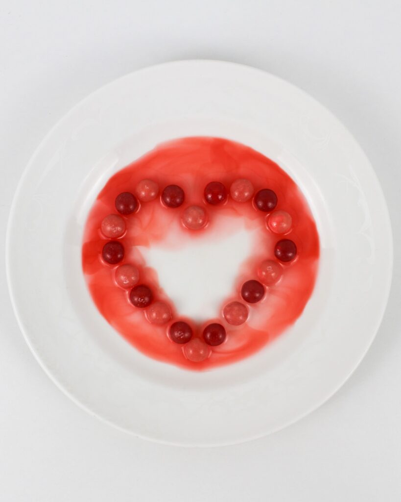 Skittles, arranged in the shape of a heart on a small plate, with the colors leaching out.