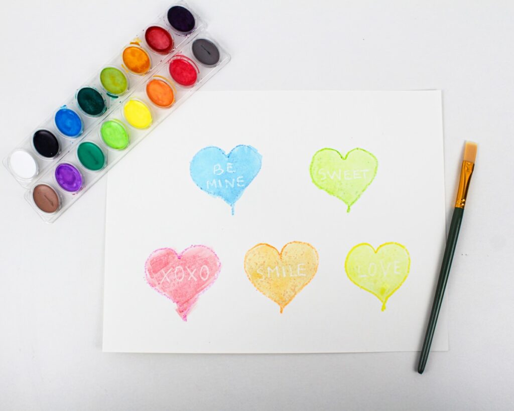 Painted hearts with white words and conversation heart candies placed on top.