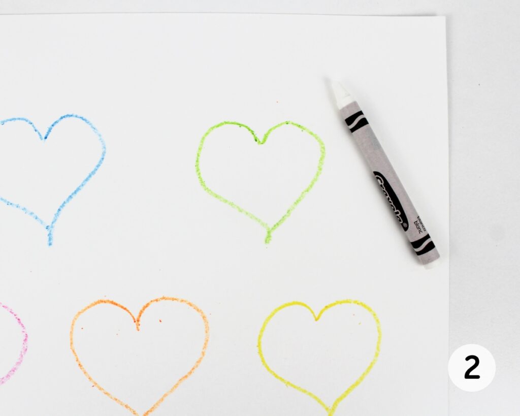 Closeup of a green heart outline with a white crayon next to it.