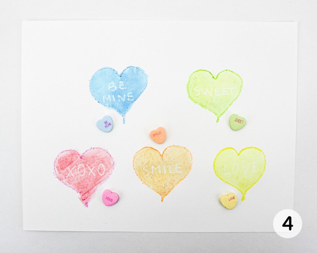 Painted hearts with white words and conversation heart candies placed on top.