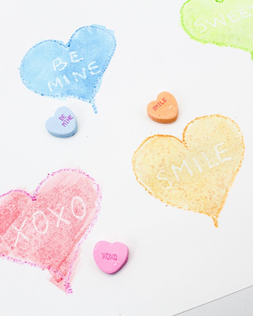 Painted hearts with white words and conversation heart candies placed on top.