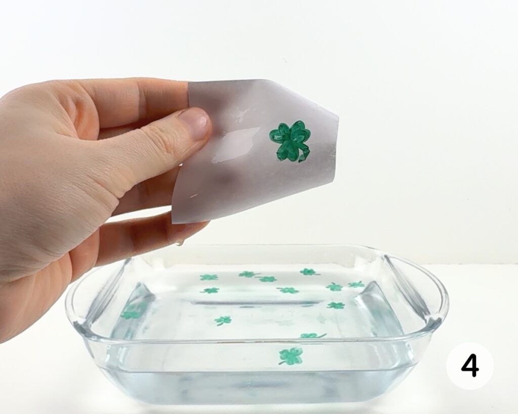 Hand holding up a piece of paper with a shamrock drawing stuck to it.