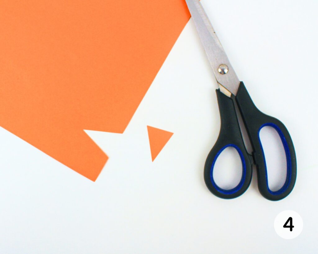 Scissors cutting a small triangle from orange construction paper.