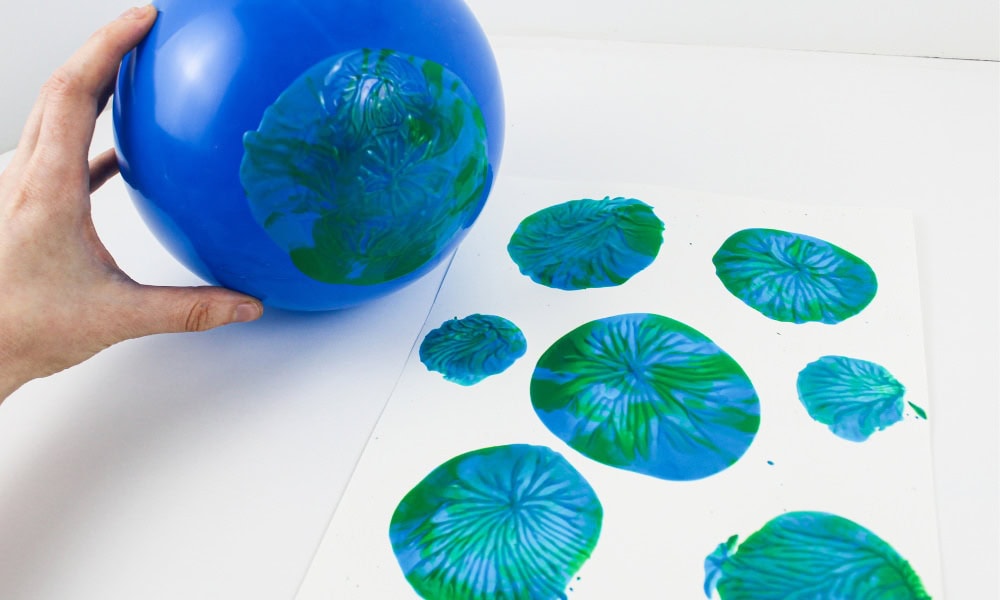 Balloon dipped in paint, creating blue-and-green prints on a sheet of cardstock.