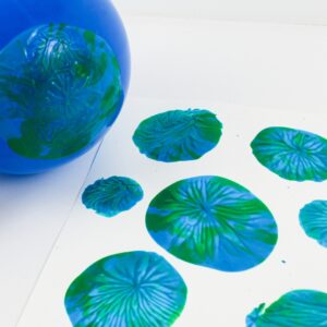Balloon dipped in paint, creating blue-and-green prints on a sheet of cardstock.