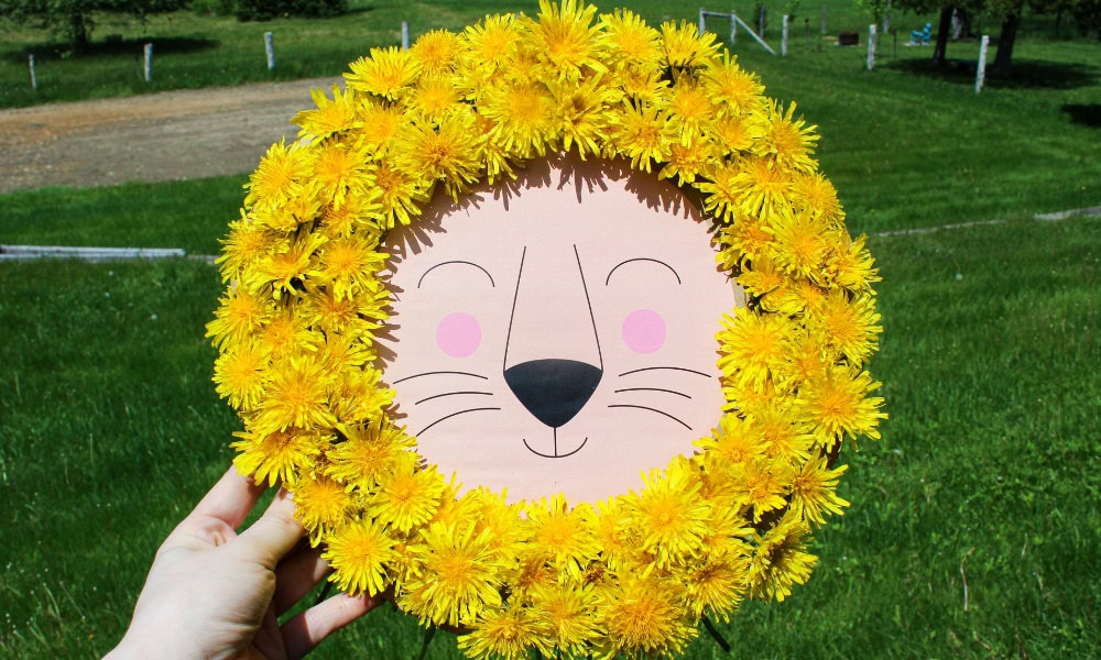 Hand holding up a lion craft with a mane made from yellow dandelions.