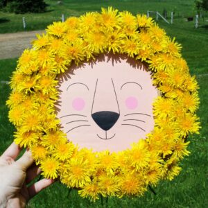Hand holding up a lion craft with a mane made from yellow dandelions.