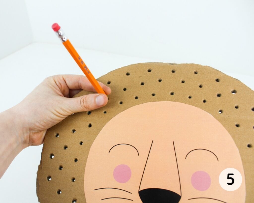 Pencil poking holes into the cardboard circle with the lion face template.