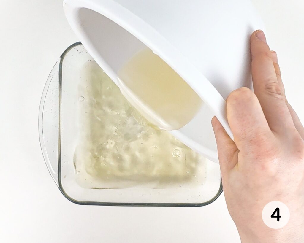 Hand pouring gelatin mixture into a square baking dish.